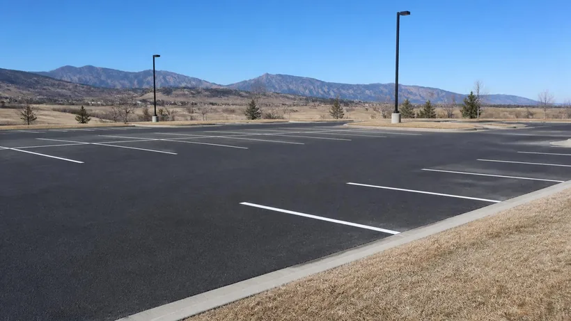 Empty commercial parking lot with fresh white stall lines, a concrete curb and dry winter grass, Front Range foothills on the horizon